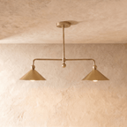 Clérachic chandelier in a warm satin brass finish, twin cone shades suspended from a slender ceiling rod.