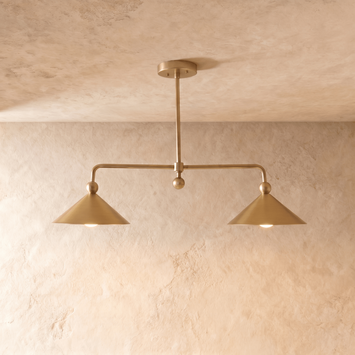 Clérachic chandelier in a warm satin brass finish, twin cone shades suspended from a slender ceiling rod.