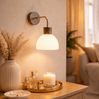 A Clérachic wall light glows warmly over a tray of candles and scent bottles on a bedside dresser.