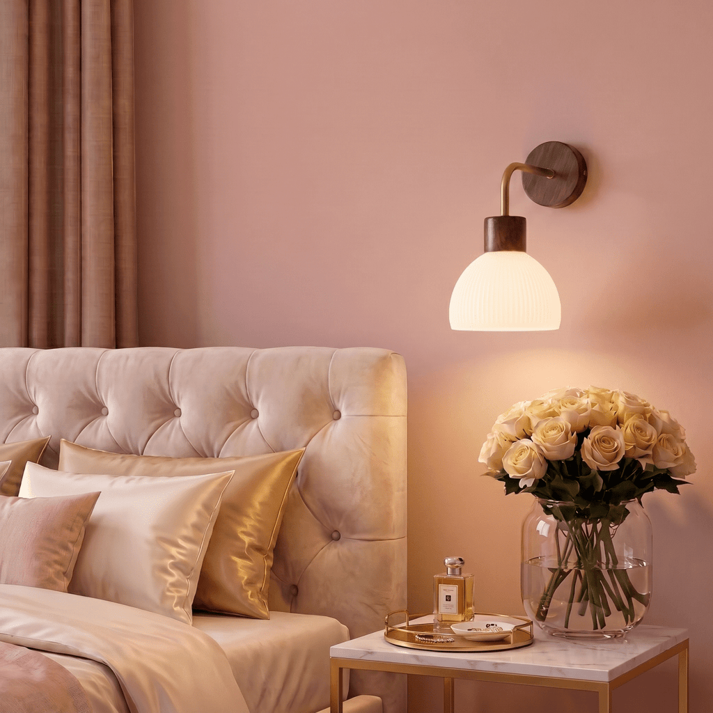 A Clérachic wall light glows beside a tufted headboard, lighting a marble nightstand with a rose bouquet.