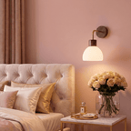 A Clérachic wall light glows beside a tufted headboard, lighting a marble nightstand with a rose bouquet.