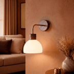This Clérachic wall light glows beside a sofa nook, lighting a vase of greenery on a wooden console.