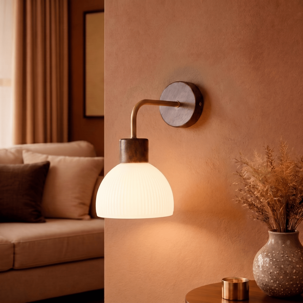 This Clérachic wall light glows beside a sofa nook, lighting a vase of greenery on a wooden console.