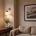 A Clérachic wall light glows warmly above a console table, its opal glass dome lit beside framed art.