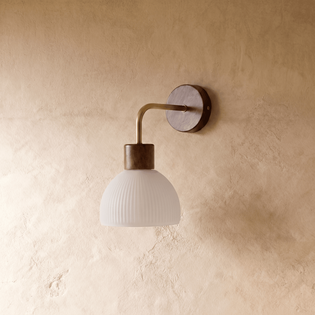 A Clérachic wall light extends a curved brass arm from a bronze base to a fluted white glass dome shade.