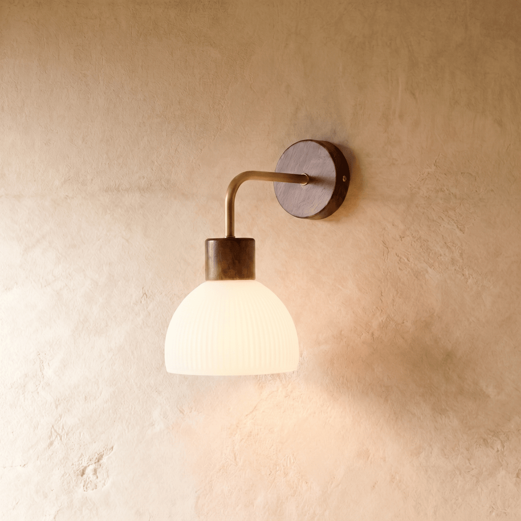 This Clérachic wall light pairs a dark bronze wall plate with a ribbed opal glass dome on a curved brass arm.