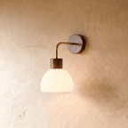 This Clérachic wall light pairs a dark bronze wall plate with a ribbed opal glass dome on a curved brass arm.
