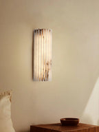Alabaster wall light glowing beside a bed for reading