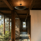 Clérachic matte black flush ceiling light mounted in a timber-beamed hallway overlooking a stone pillar and hills.