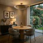 Clérachic brass flush ceiling light glowing above a round dining table with framed botanical prints nearby.