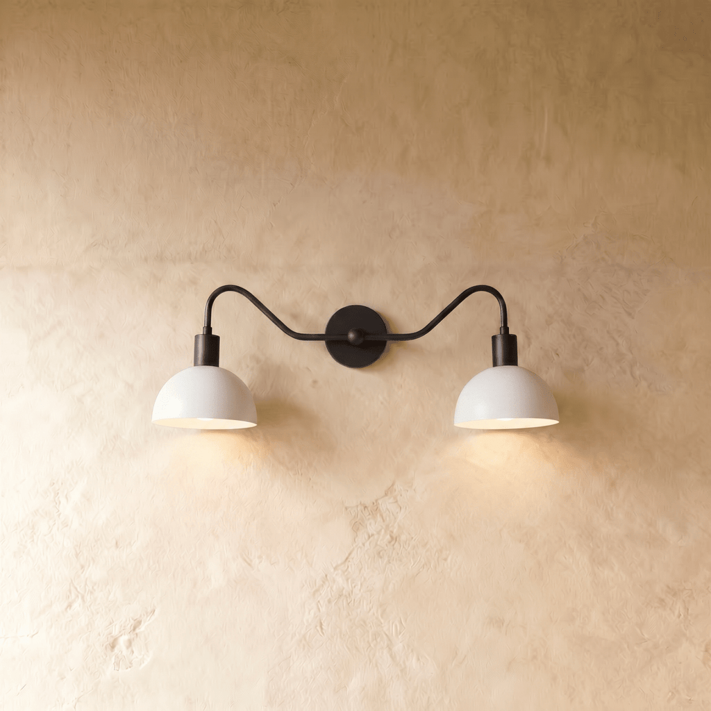 Clérachic twin wall light in black, lit, the dark rod drawn across the pale wall above two glowing white domes.
