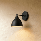 A matte black Clérachic wall lamp with a bell-shaped shade on a straight arm against a plaster wall.
