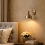A vintage brass Clérachic wall lamp lights a bedroom nightstand holding roses and a glass perfume bottle.