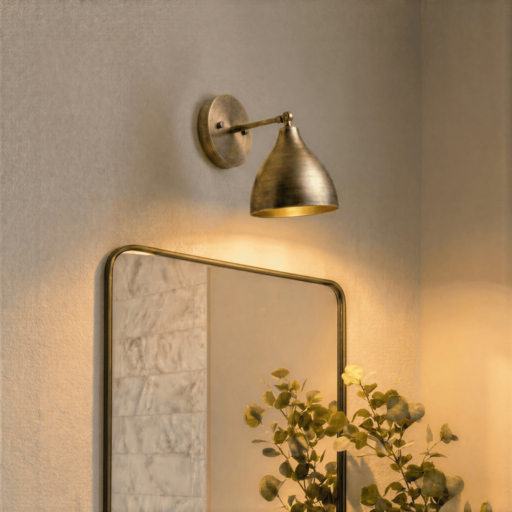 A vintage brass Clérachic wall lamp lights a bathroom mirror framed in brass beside eucalyptus stems.