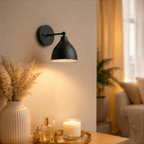 This black Clérachic wall lamp lights a side table set with a candle, perfume bottles and a pampas vase.
