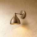 Clérachic wall lamp in polished brass, its bell-shaped shade angled down from a slim wall-mounted arm.
