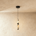 Clérachic marble column pendant light lit against a plastered wall corner, its cord dropping from a round black ceiling canopy.