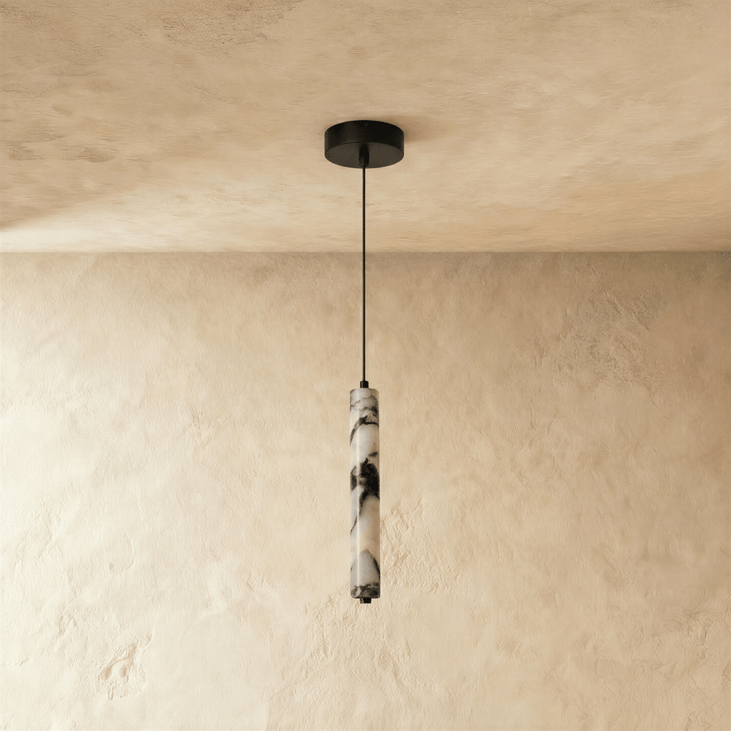 Clérachic marble column pendant light shown unlit, its grey-black veining reading as cold stone against a warm plastered wall.