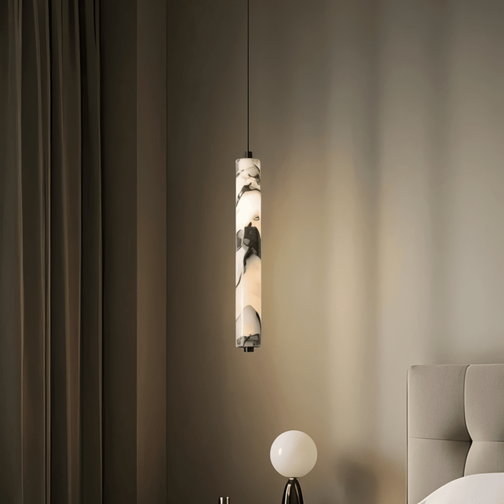 Clérachic marble pendant light lit against drawn curtains, hanging beside a round white globe table lamp and an upholstered headboard.
