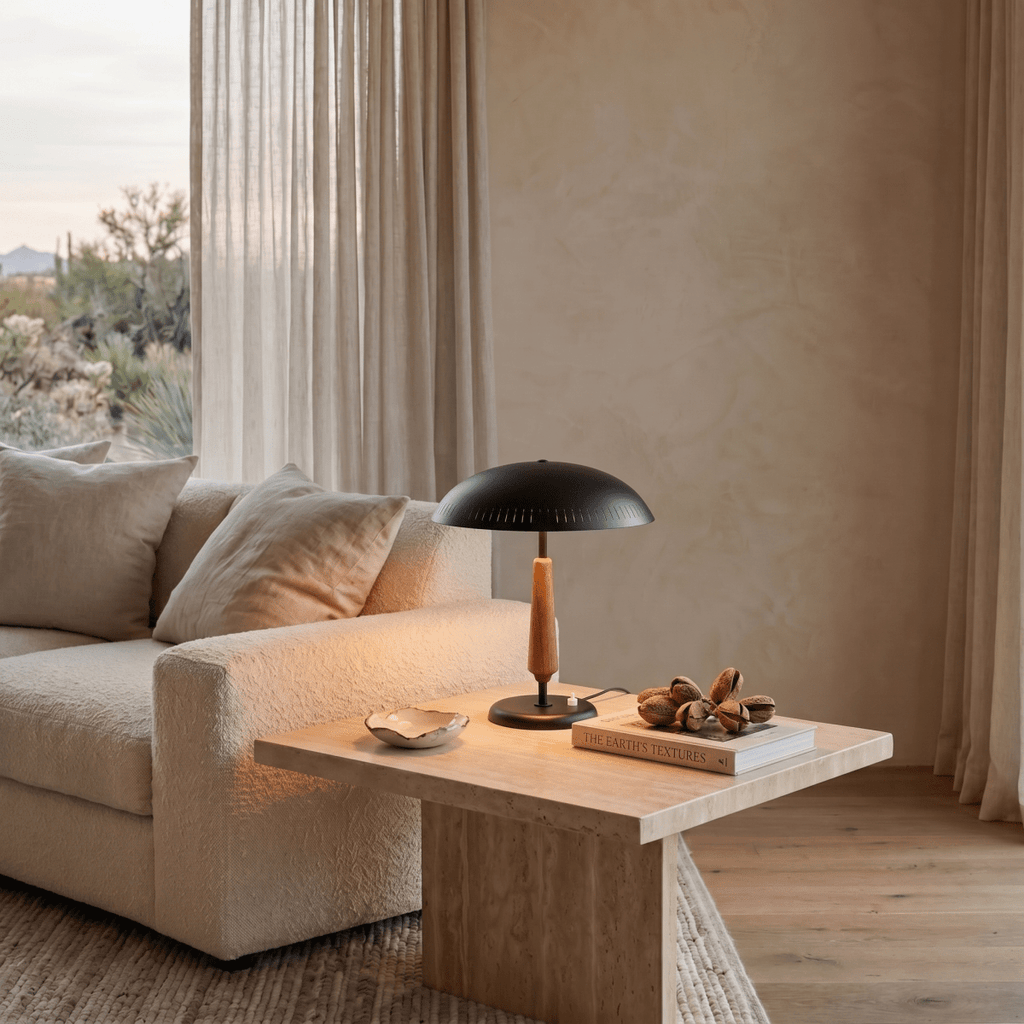 Clérachic matte black table lamp glowing on a travertine side table beside a beige sofa and desert-view window.