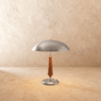 Clérachic table lamp in a bright chrome finish, its dome shade and turned wood stem set on a plaster surface.