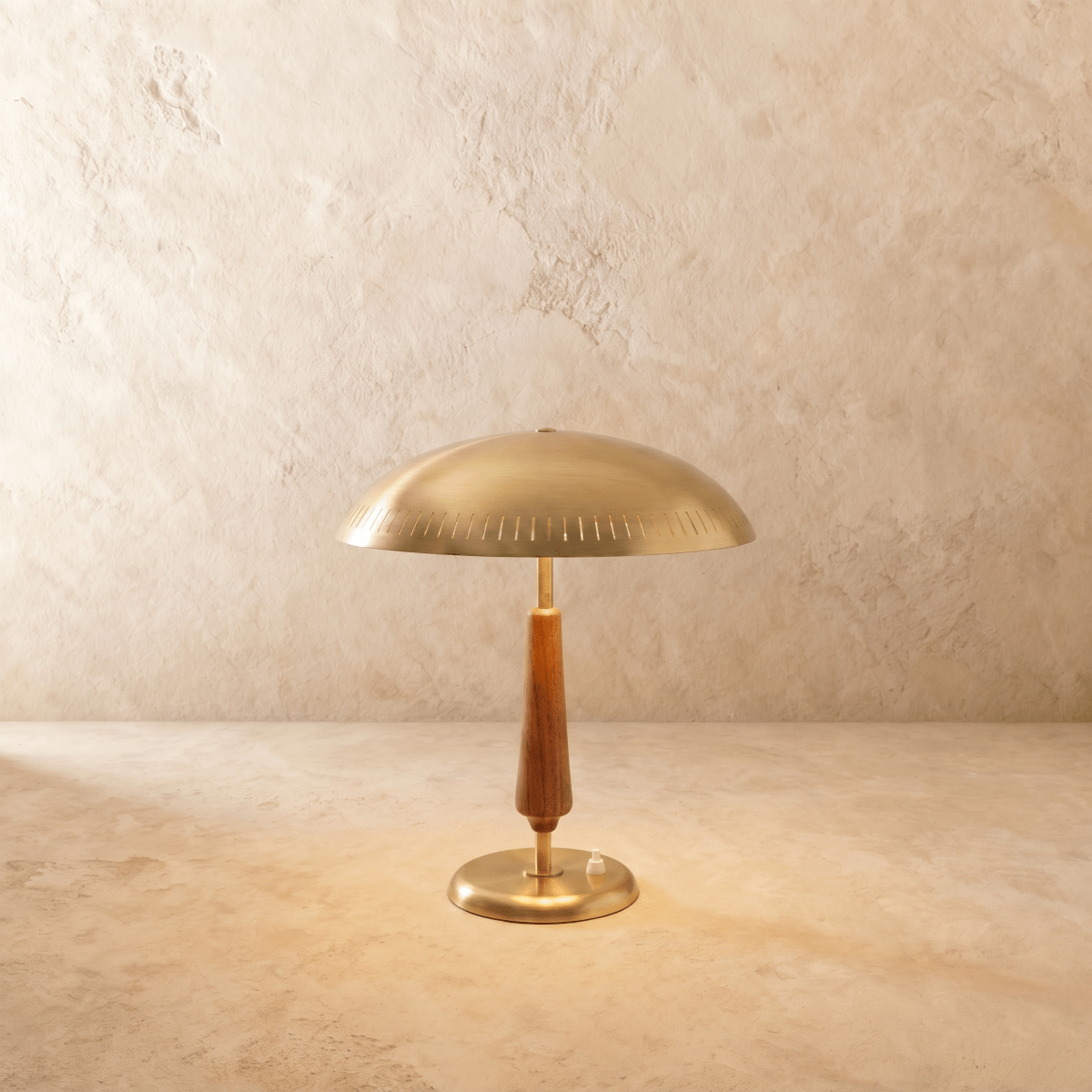 Clérachic table lamp in a brighter brass finish, its dome shade and turned wood stem set on a plaster surface.
