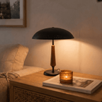 Clérachic matte black table lamp glowing on a wooden side table beside a lit candle and a framed print.