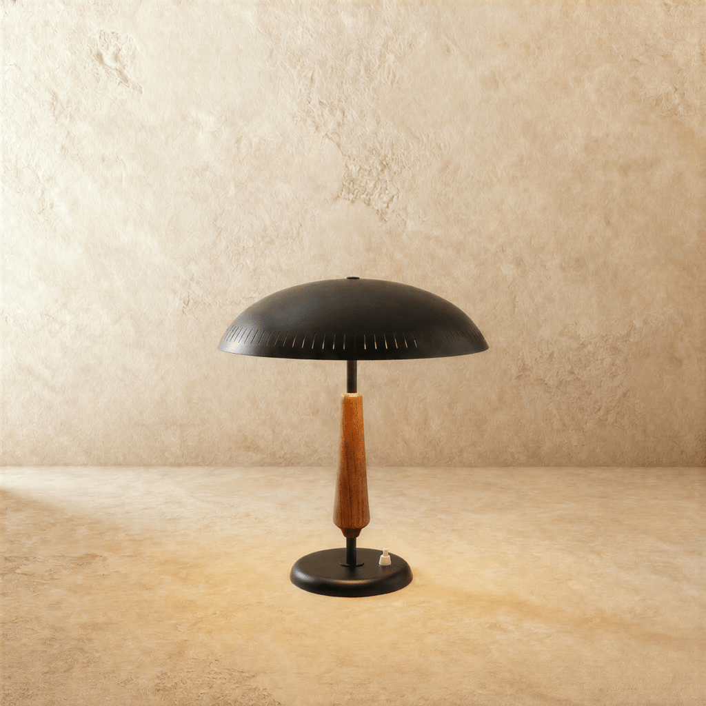 Clérachic table lamp in matte black with a turned walnut stem, its dome shade shown on a plaster surface.