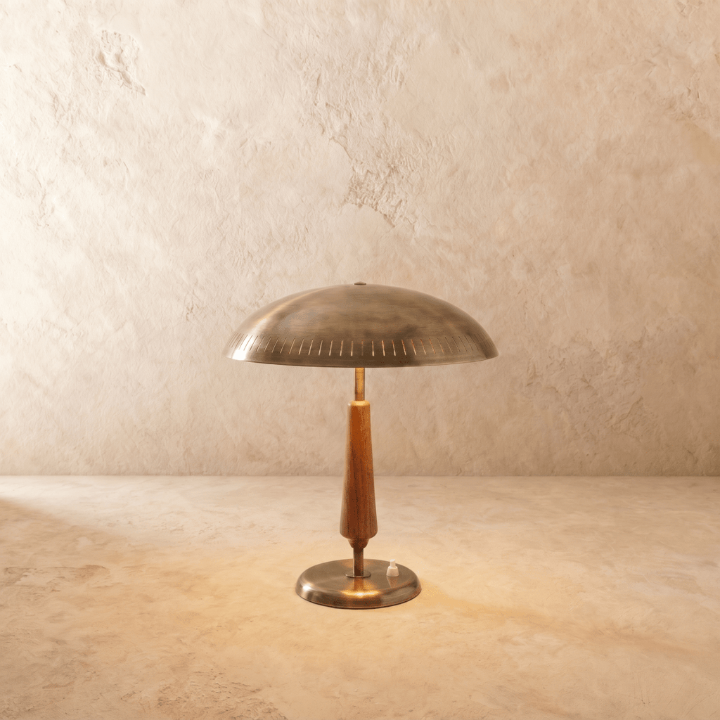 Clérachic table lamp in vintage brass with a turned walnut stem, its wide dome shade shown on a plaster surface.