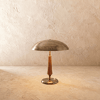 Clérachic table lamp in vintage brass with a turned walnut stem, its wide dome shade shown on a plaster surface.