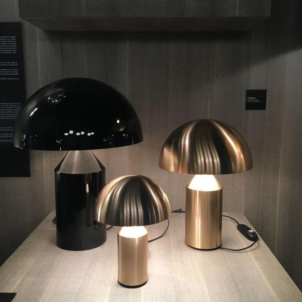 Three table lamps in black, gold, and bronze on a wooden surface with a dark background.