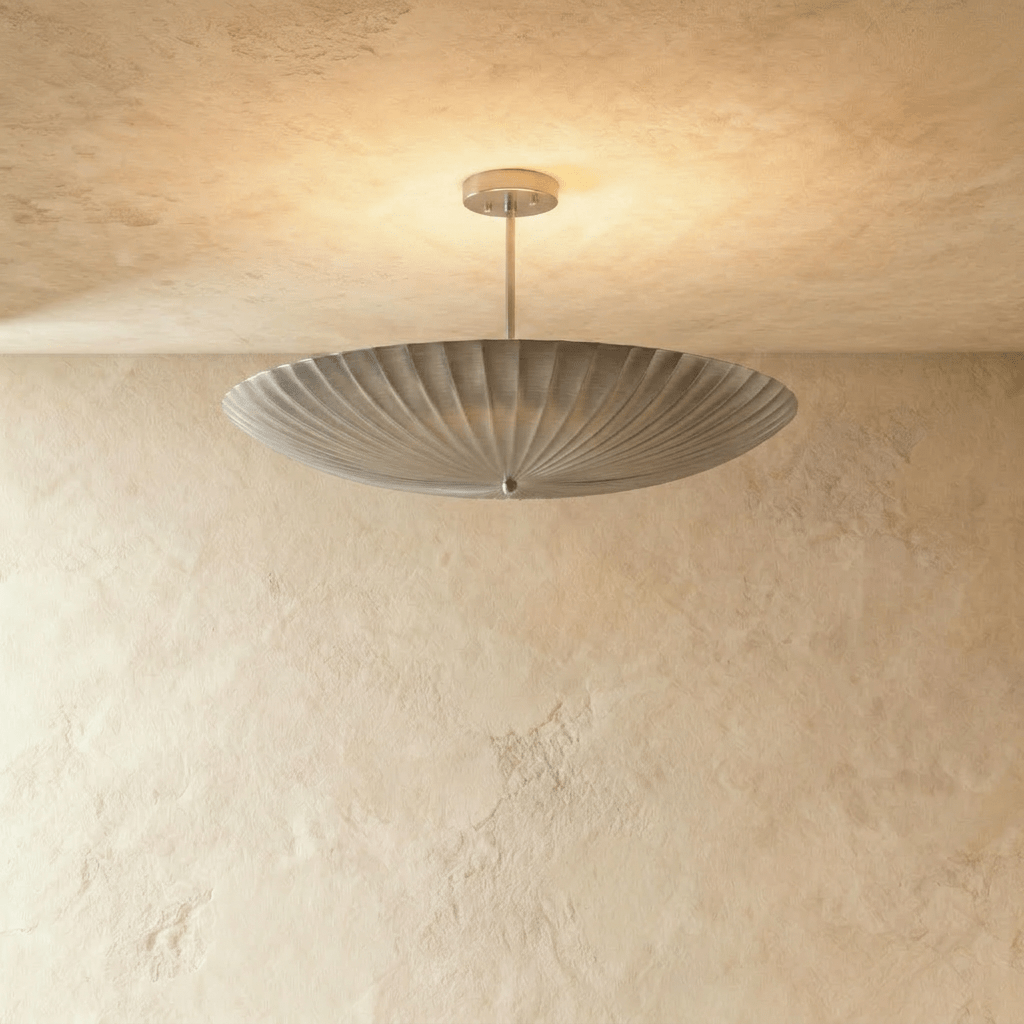 Clérachic pendant light in chrome, the fluted disc shade glowing softly from beneath a plaster ceiling.