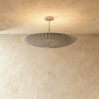 Clérachic pendant light in chrome, the fluted disc shade glowing softly from beneath a plaster ceiling.
