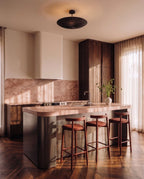 Clérachic pendant light in matte black hung above a kitchen island with pink marble and walnut cabinetry.