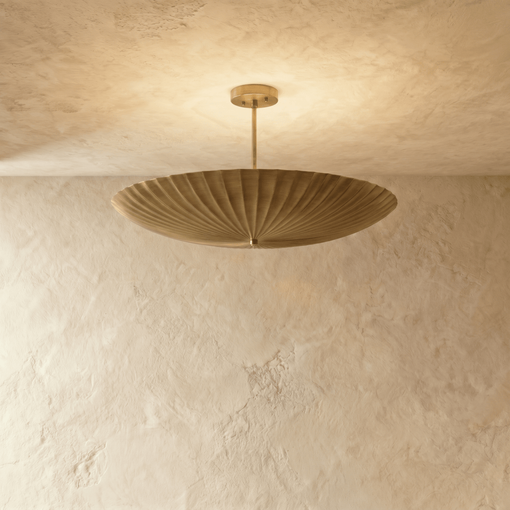 Clérachic pendant light in a warm satin brass finish, the fluted disc shade glowing from beneath.