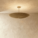 Clérachic pendant light in a warm satin brass finish, the fluted disc shade glowing from beneath.