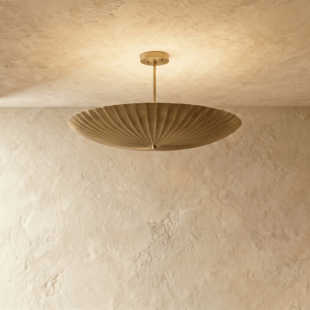 Clérachic pendant light in a warm satin brass finish, the fluted disc shade glowing from beneath.