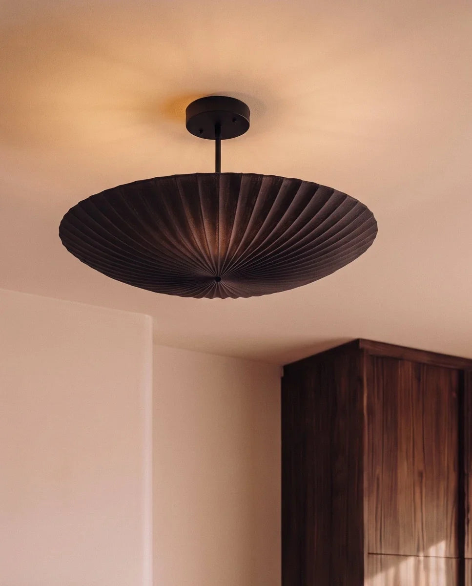 Clérachic pendant light in matte black glowing in a bedroom corner beside a tall walnut wardrobe.