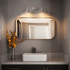 Clérachic chrome double-head wall sconce mounted above a rectangular mirror beside a black heated towel rail.