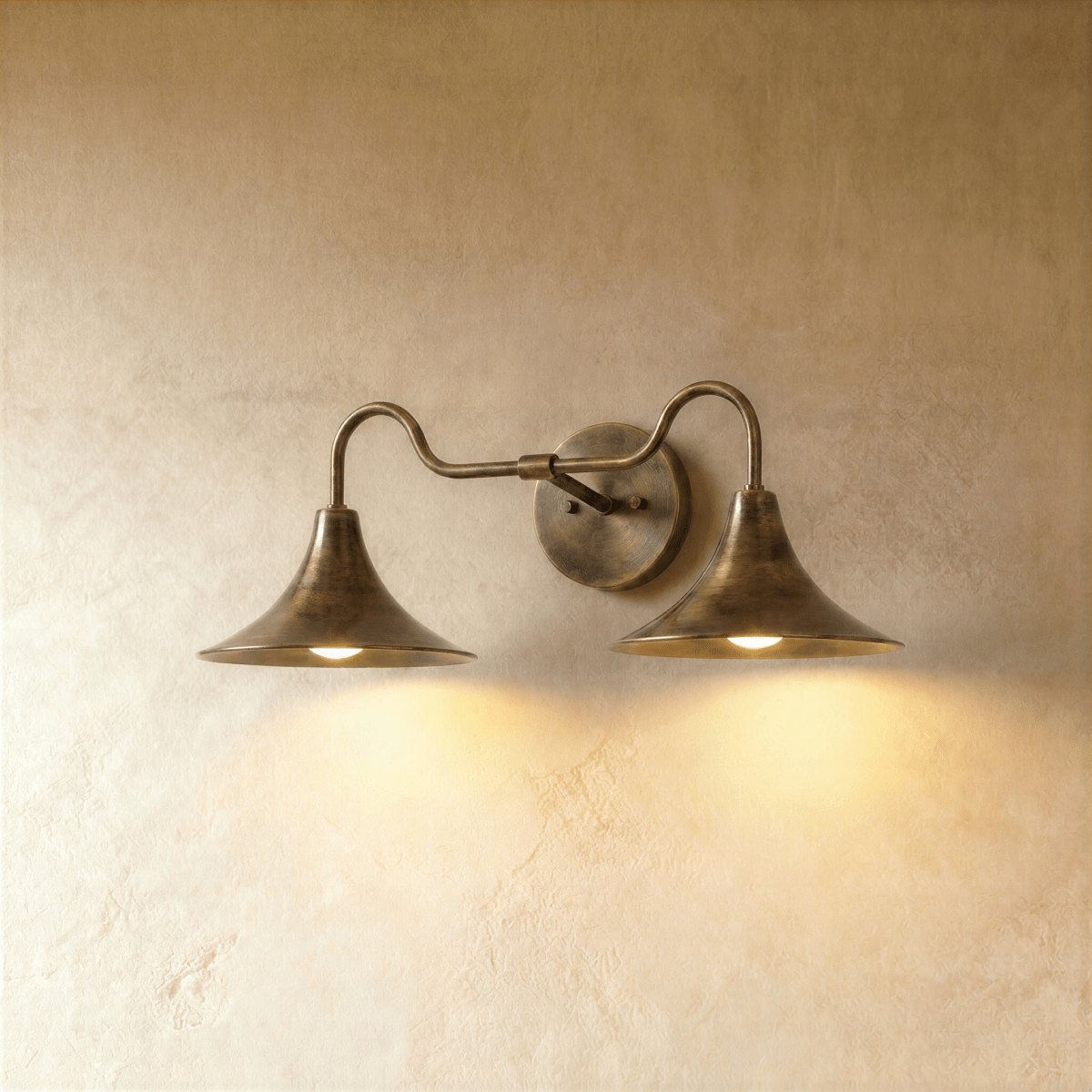 Clérachic double-head wall sconce in vintage brass, its trumpet shades curving outward against a plaster wall.