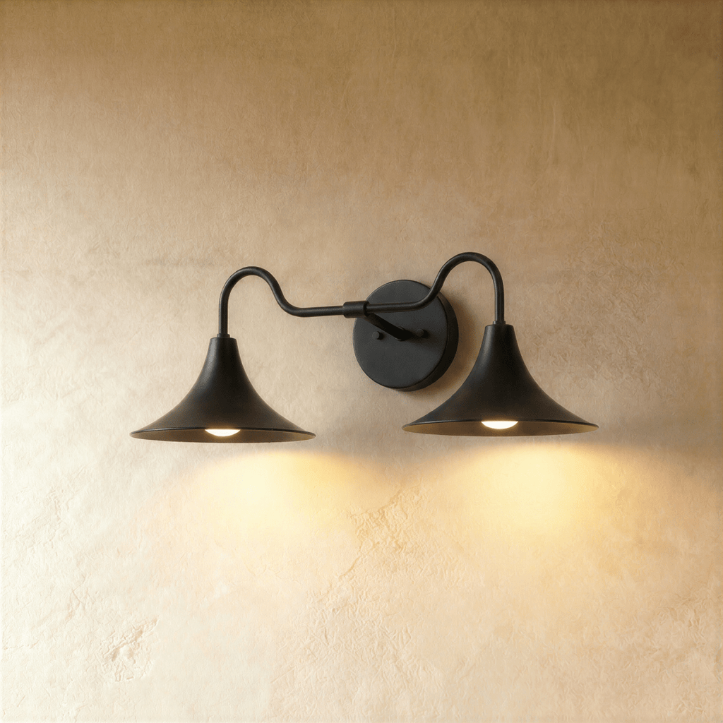 Clérachic double-head wall sconce in matte black, its trumpet shades curving outward against a plaster wall.