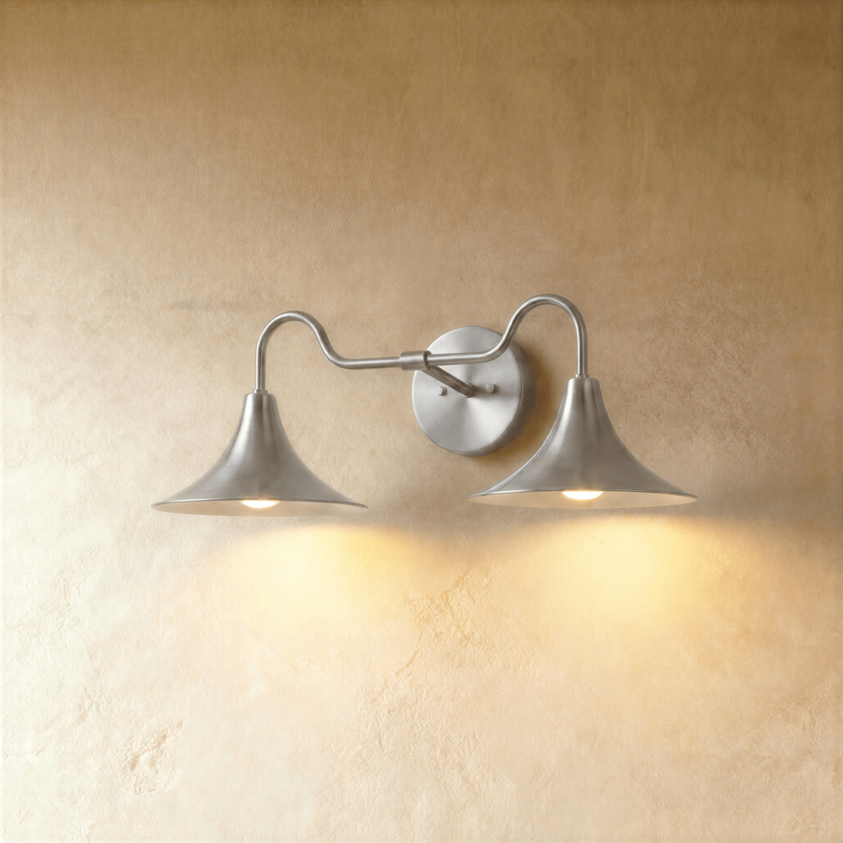 Clérachic double-head wall sconce in a bright chrome finish, its trumpet shades curving outward on a plaster wall.
