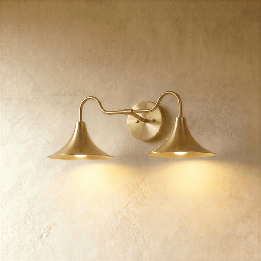 Clérachic double-head wall sconce in a brighter brass finish, its trumpet shades curving outward on a plaster wall.