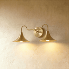 Clérachic double-head wall sconce in a brighter brass finish, its trumpet shades curving outward on a plaster wall.