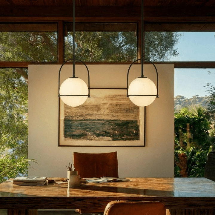 Clérachic globe pendant lights in matte black, a pair hung above a wood table between tan leather chairs and a framed painting.
