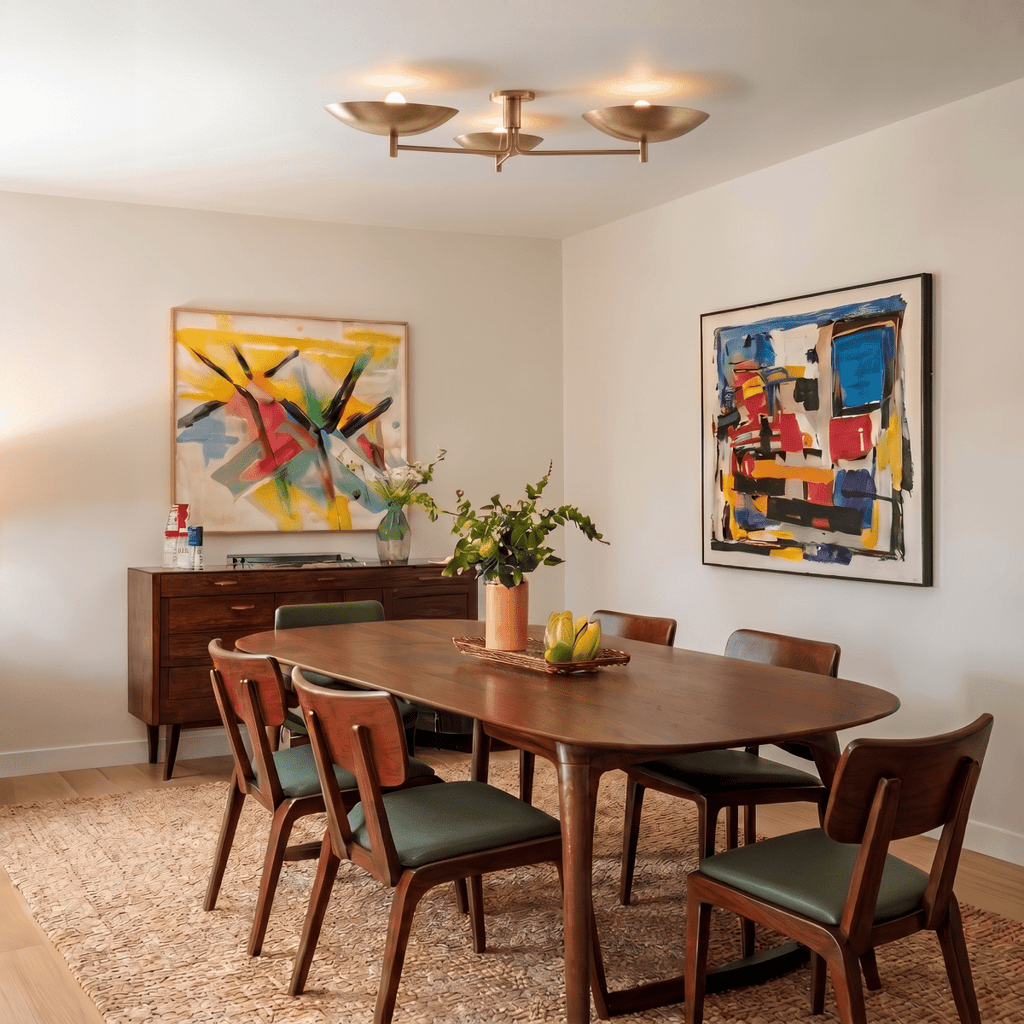 Clérachic ceiling light in brass over a walnut dining table framed by two colorful abstract paintings.