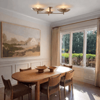 Clérachic ceiling light in brass glowing above a dining table set beneath a large landscape painting.
