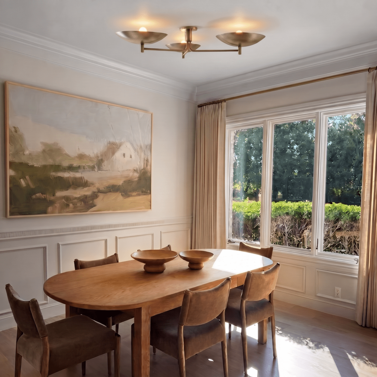 Clérachic ceiling light in brass glowing above a dining table set beneath a large landscape painting.