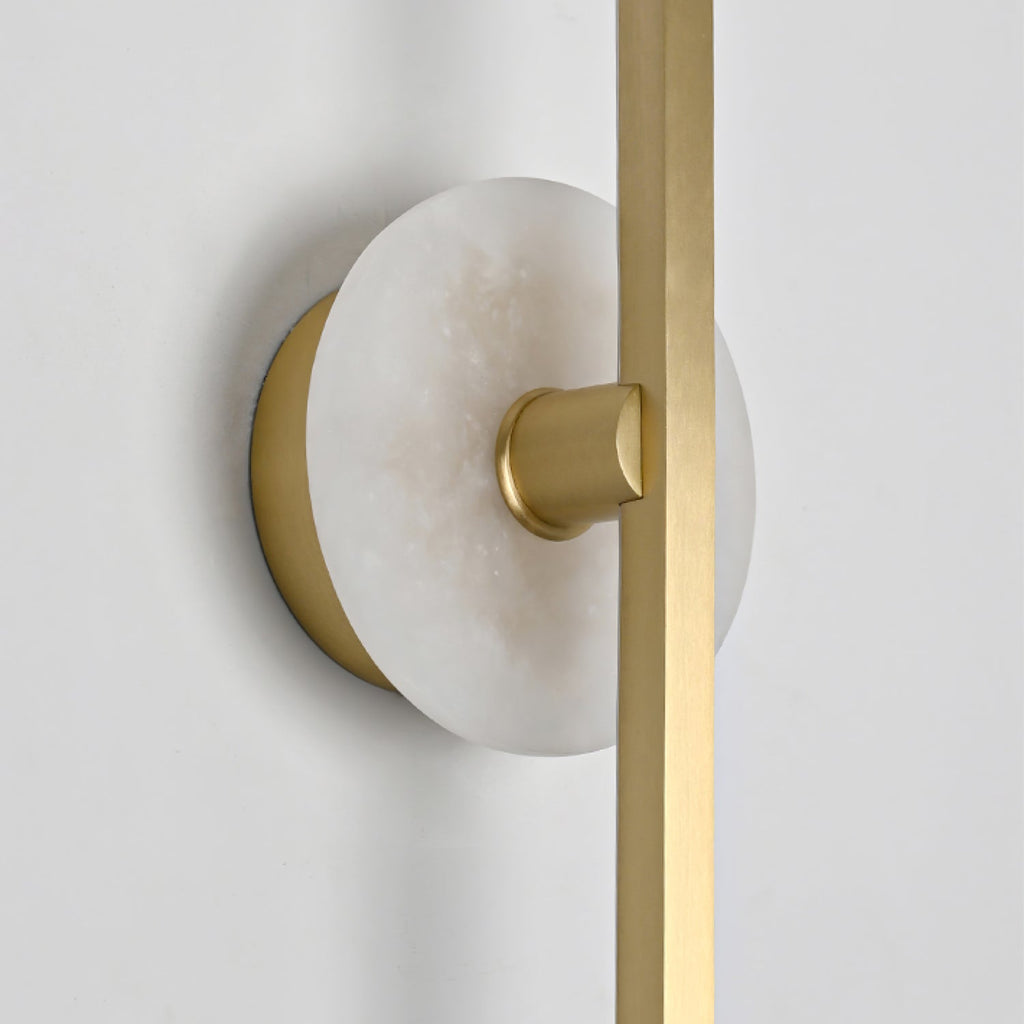 Close-up of a Clérachic wall sconce's alabaster disc and brass mounting point, photographed against a plain wall.