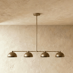 Clérachic four-dome bar pendant light in aged brass, hung against bare plaster with all four rims sitting at one height.